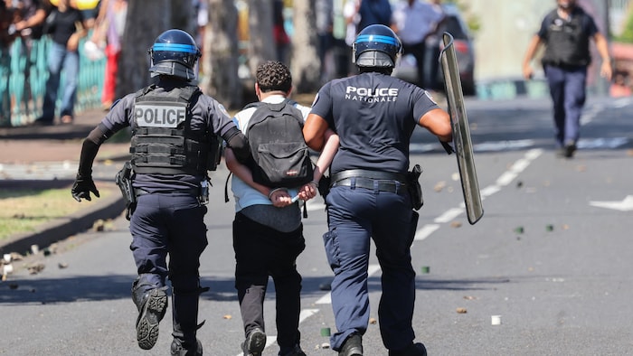 Des policiers français en tenue antiémeute interpellent un manifestant lors de manifestations étudiantes à Saint-Pierre, sur l'île française d'outre-mer de La Réunion, le 2 octobre 2026. 